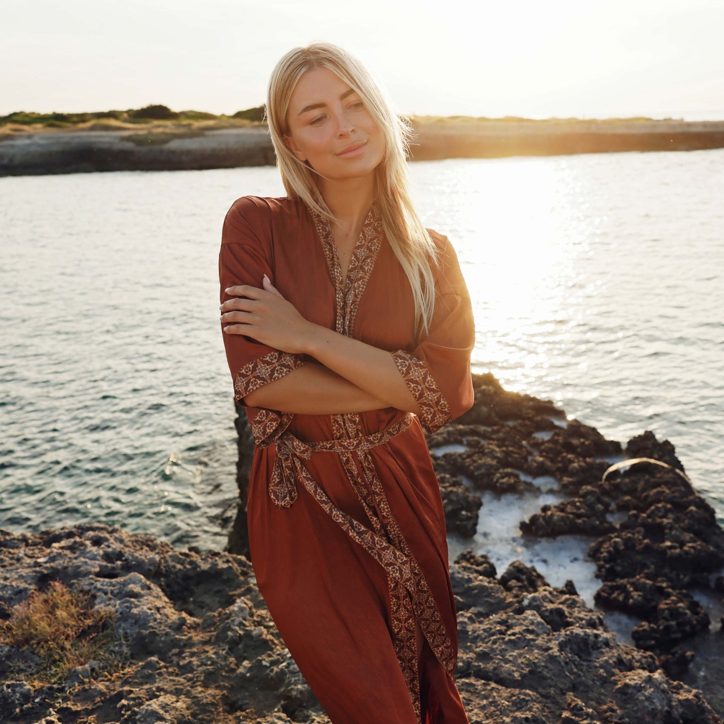Vrouw in bruine satijnen kimono op het strand bij zonsondergang
