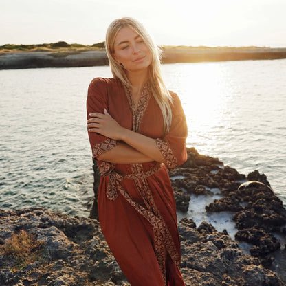 Vrouw in bruine satijnen kimono op het strand bij zonsondergang