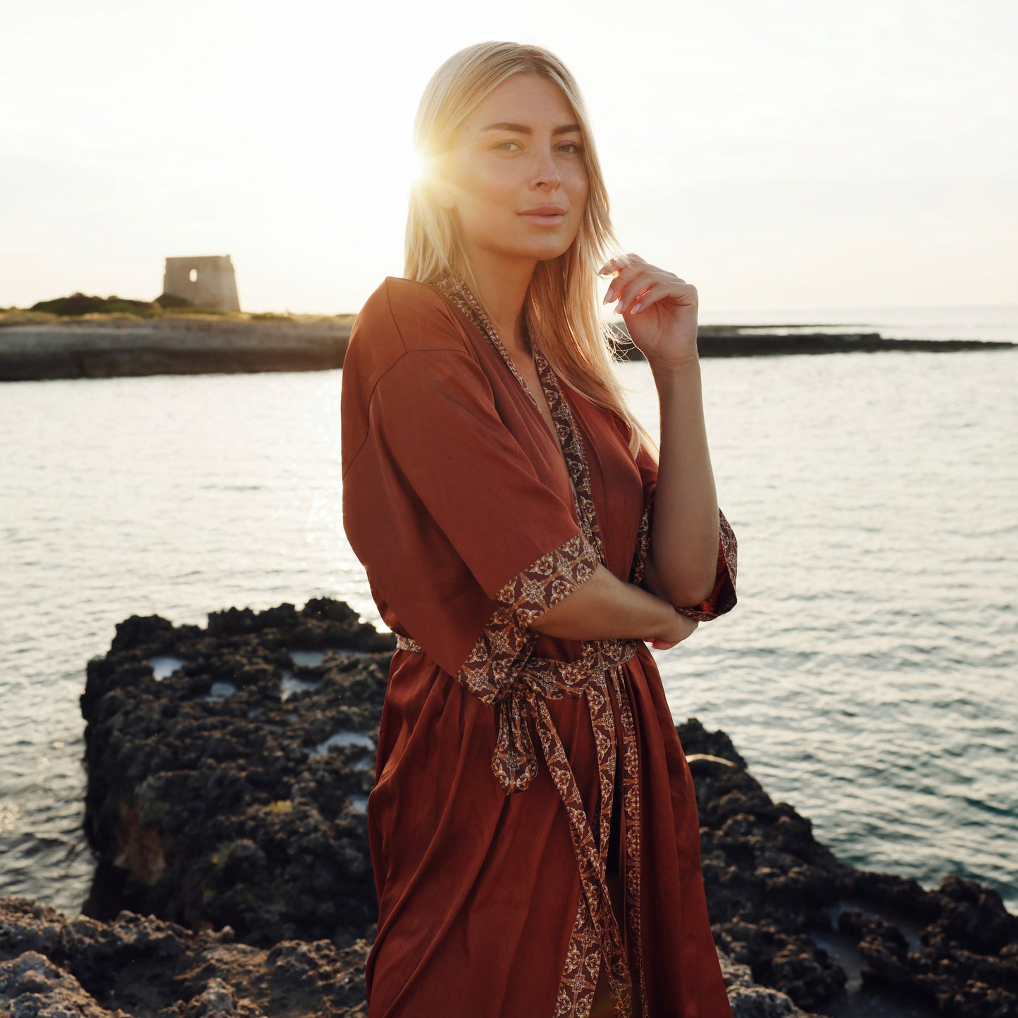 Vrouw in bruine satijnen kimono op het strand met zonsondergang